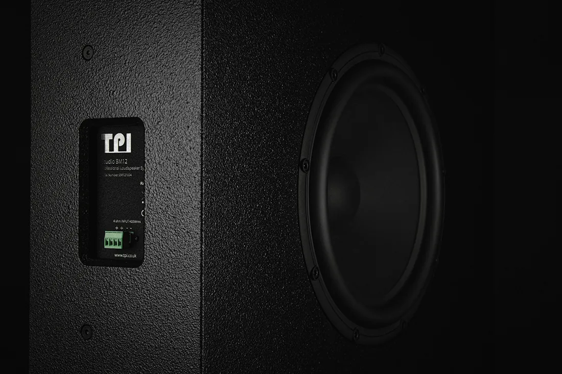 Close-up of a black Type. BM-12 cabinet in low light: the TPI badge and connection panel beside a large driver.