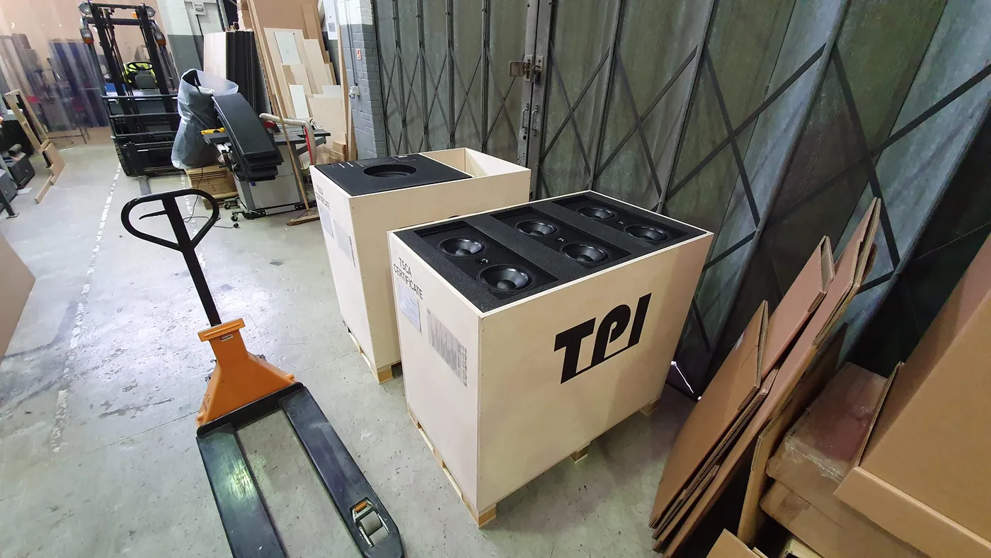 Plywood shipping crates on a pallet truck in a workshop, one open to show its foam insert.