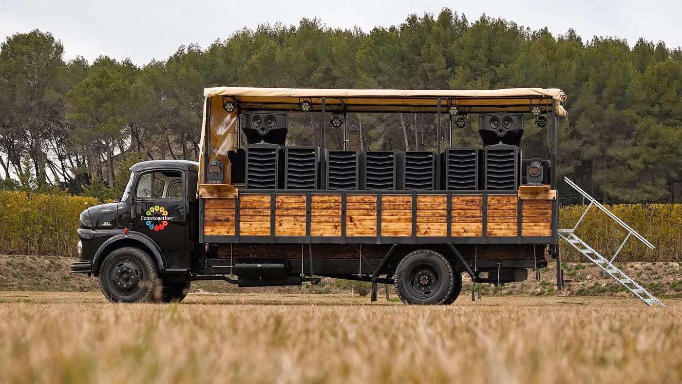 A converted 1965 Mercedes truck in a field in Provence, its deck lined with MFR cabinets under a canopy.