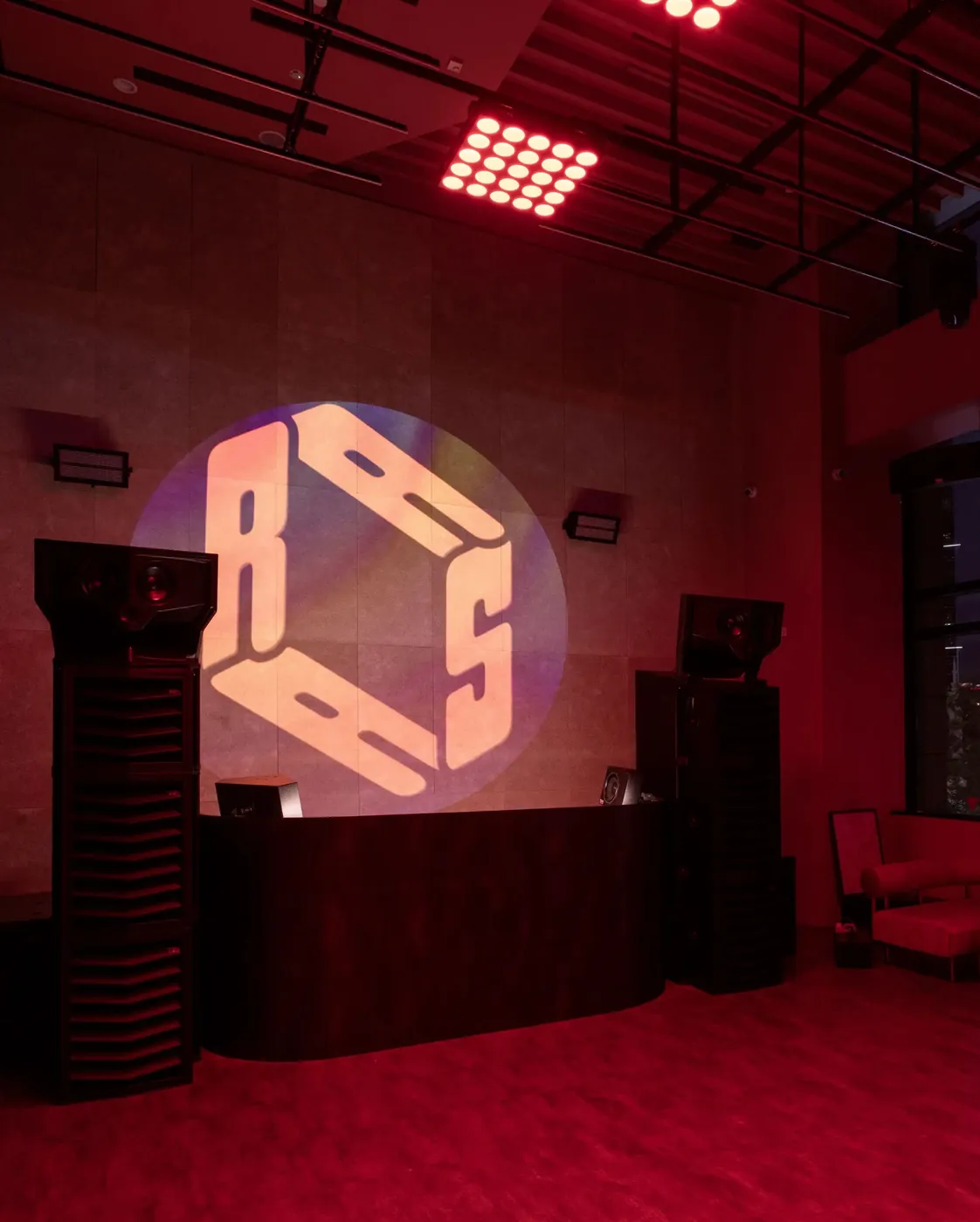 Two tall Type. MFR stacks either side of the DJ booth at RASA Space, the club's logo projected on the wall behind, in red light.