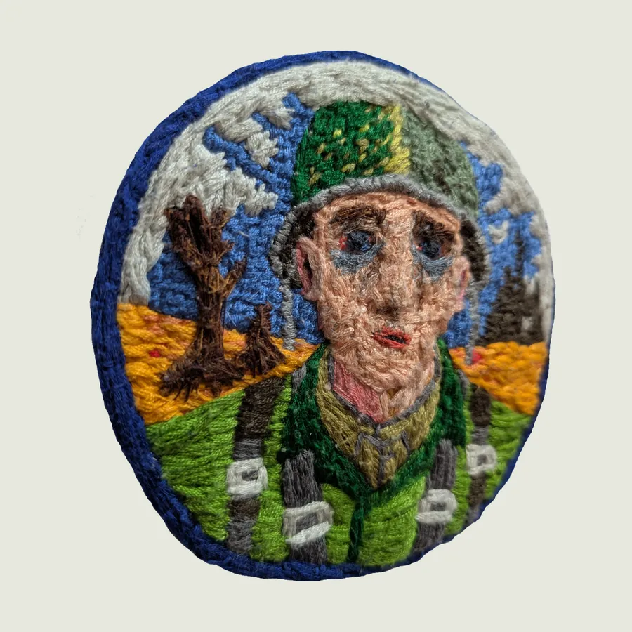 The soldier patch photographed at a low angle on white paper, showing its raised, layered stitching and the thickness of its blue edge.