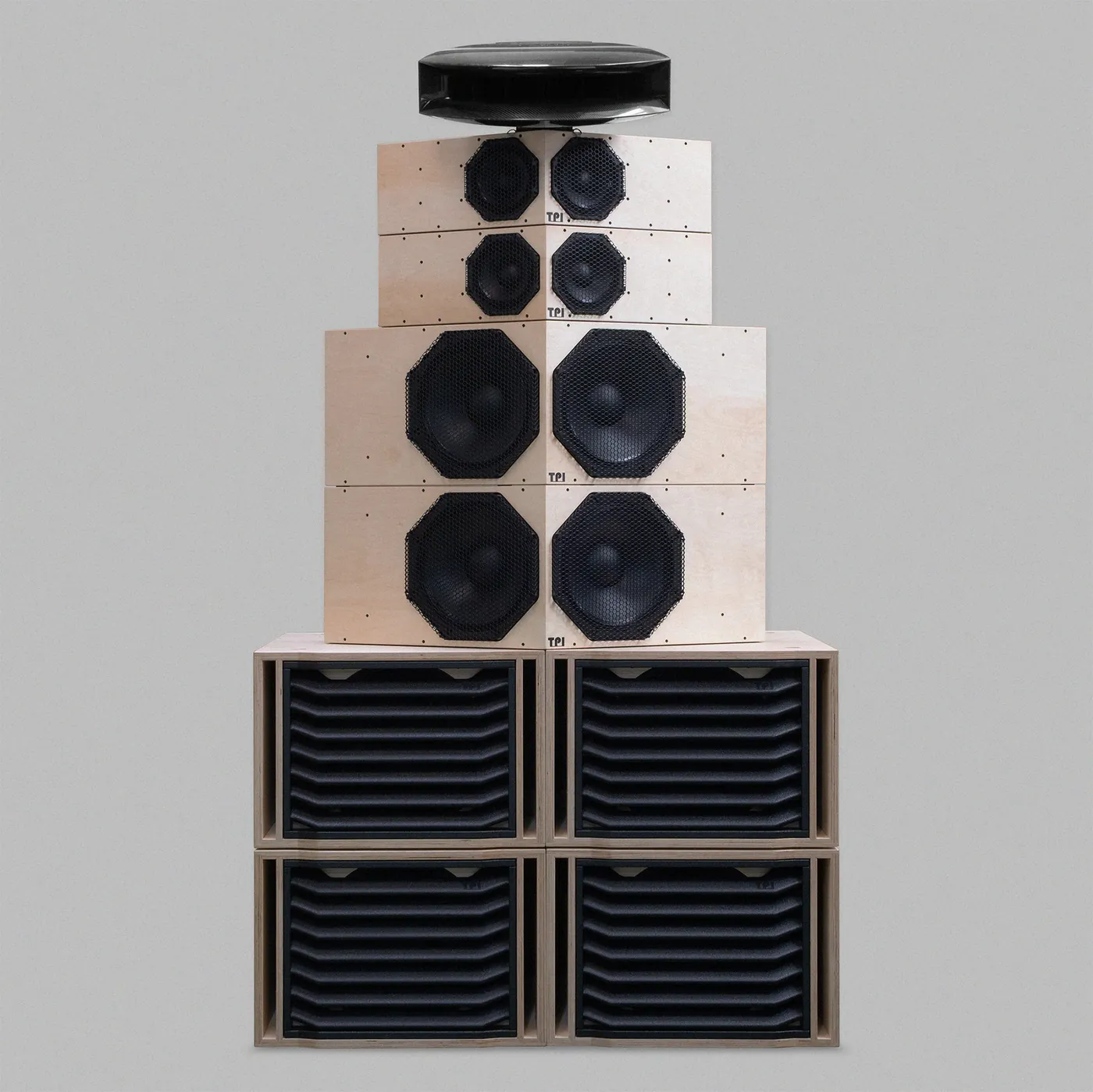 Type. TOTEM 2 in natural birch ply: slotted bass cabinets two by two at the base, two large V-fronted modules with octagonal driver frames, two smaller ones above, and a black horn on top.