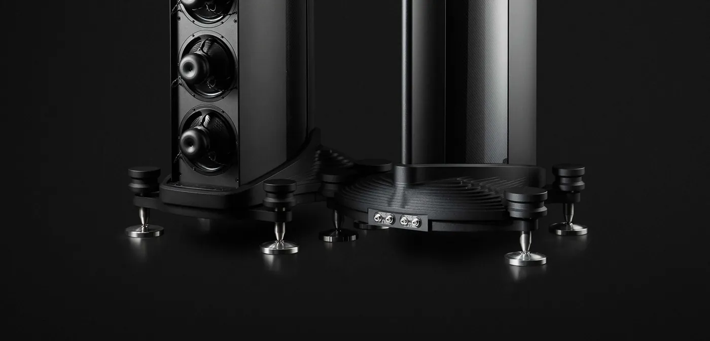 Low view of the base of an Eminence against black: the machined aluminium foot with hand-wheels and spikes, and the isobaric drive units above it.