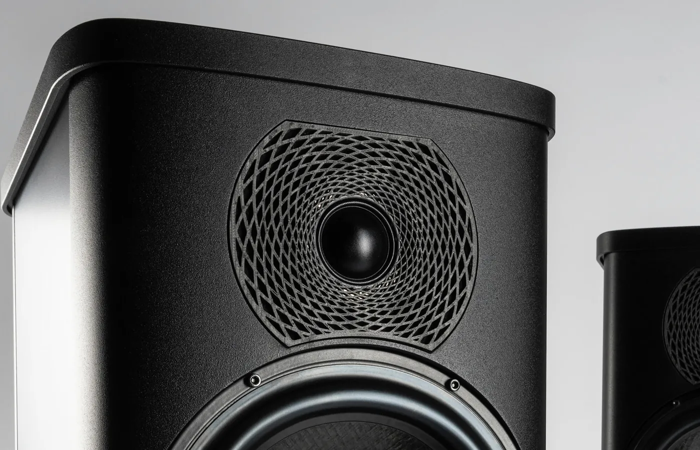 Close-up of a black Precision cabinet: a small dome tweeter set in a round faceplate patterned with a lattice of curved ribs, above a drive unit.